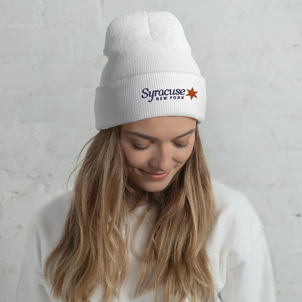 A young woman facing us wearing a white winter beanie hat embroidered with a Syracuse, NY logo